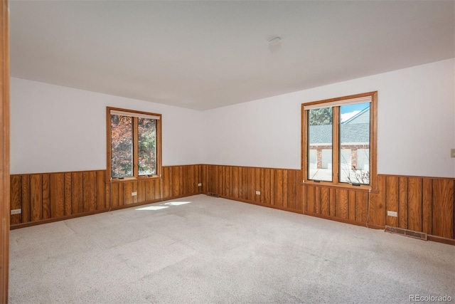 carpeted spare room featuring wood walls, visible vents, and a wainscoted wall