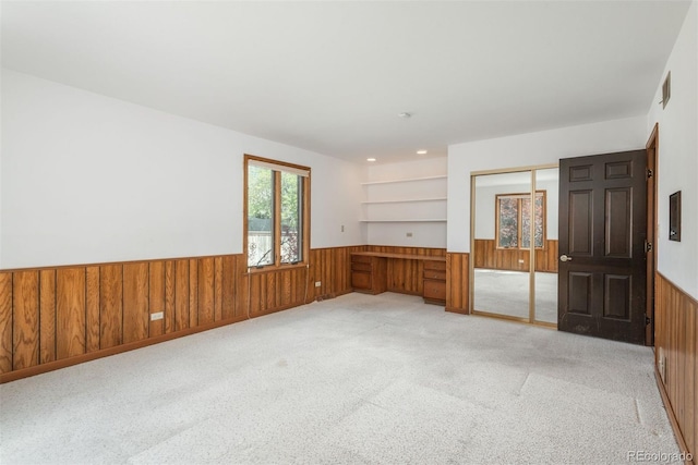 empty room with visible vents, wood walls, a wainscoted wall, and light carpet