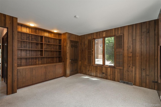 carpeted empty room featuring wood walls and visible vents