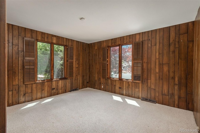carpeted spare room featuring wood walls and visible vents