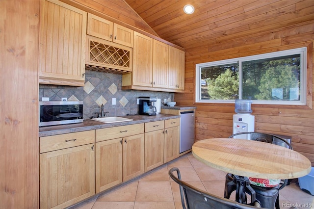 kitchen with light brown cabinetry, stainless steel appliances, sink, light tile patterned floors, and wood walls