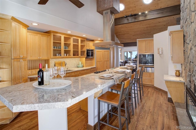 kitchen featuring a spacious island, hardwood / wood-style flooring, beamed ceiling, island exhaust hood, and stainless steel appliances