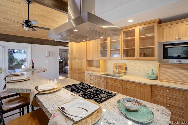 kitchen featuring decorative backsplash, gas cooktop, light stone counters, island range hood, and sink