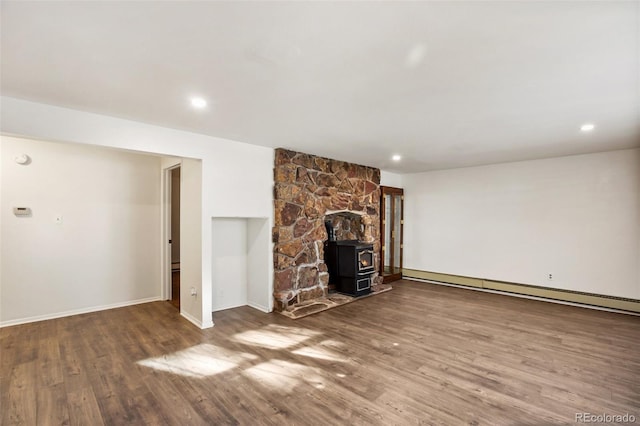 unfurnished living room featuring wood-type flooring, a wood stove, and baseboard heating