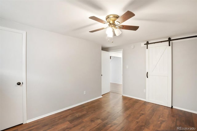 unfurnished bedroom featuring ceiling fan, a barn door, and dark hardwood / wood-style flooring