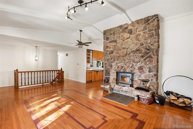 living room featuring a wood stove, ceiling fan, track lighting, and vaulted ceiling