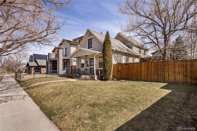 view of home's exterior with stone siding, a lawn, covered porch, and fence