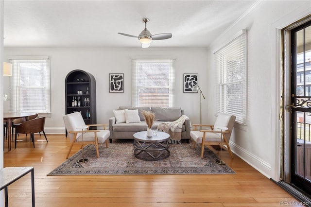 living area with ceiling fan, baseboards, light wood-style flooring, and crown molding