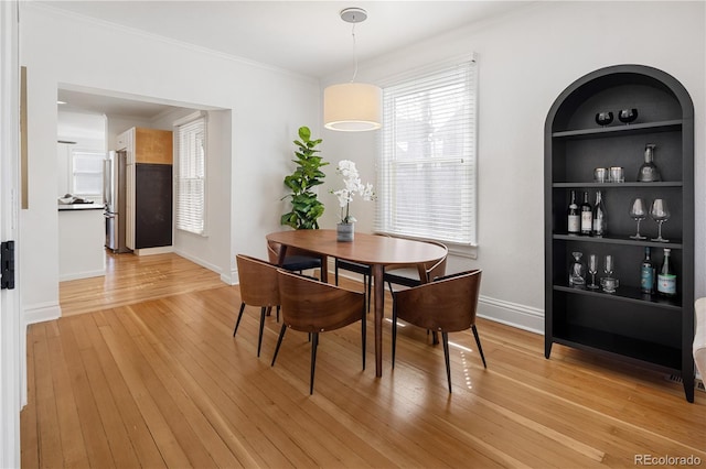 dining room with crown molding, built in shelves, light wood-style floors, and baseboards