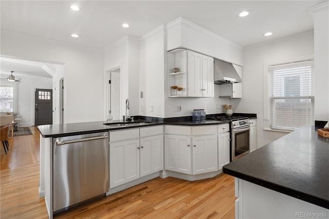 kitchen with a sink, dark countertops, stainless steel appliances, a peninsula, and wall chimney exhaust hood