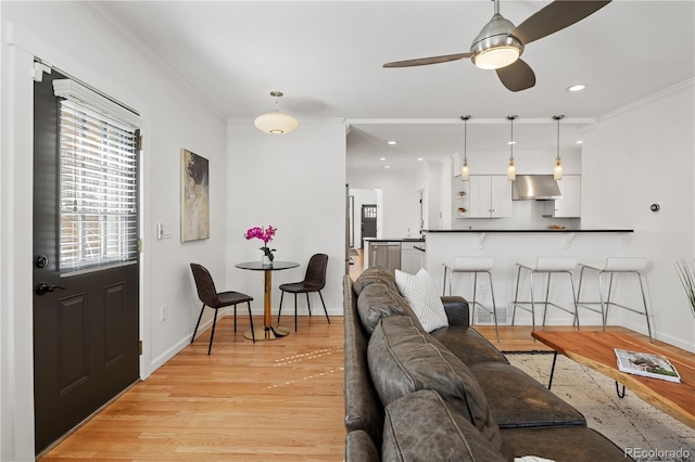 living area featuring a ceiling fan, baseboards, recessed lighting, light wood-style floors, and crown molding