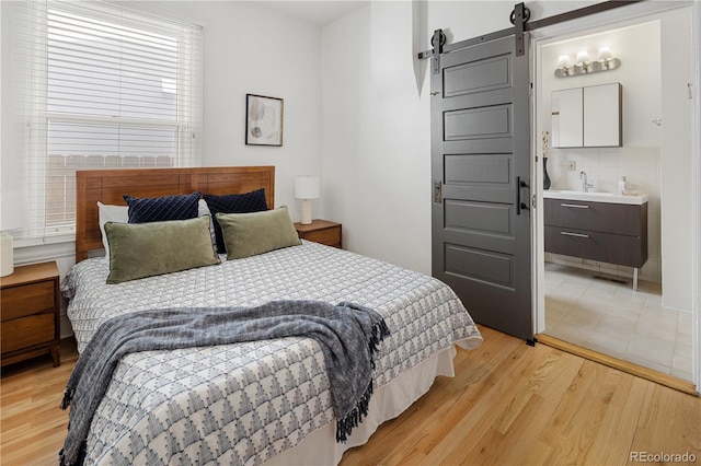 bedroom with a barn door, light wood-style flooring, and a sink