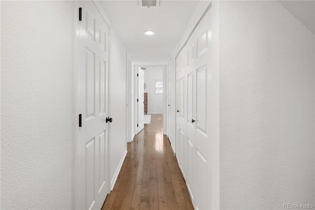 hall with visible vents, dark wood-style flooring, and a textured wall