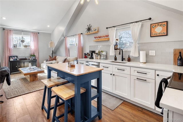 kitchen with stainless steel dishwasher, light wood-type flooring, lofted ceiling, and a sink