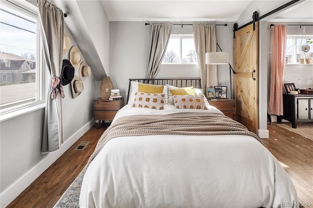 bedroom with a barn door, baseboards, visible vents, and wood finished floors