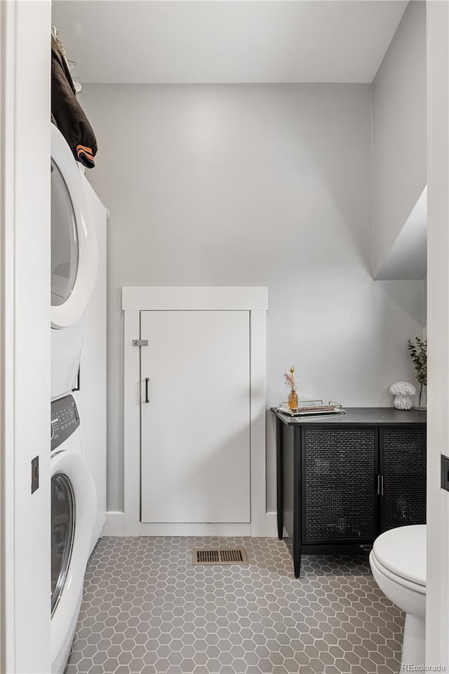 clothes washing area featuring tile patterned floors, stacked washer and dryer, and laundry area