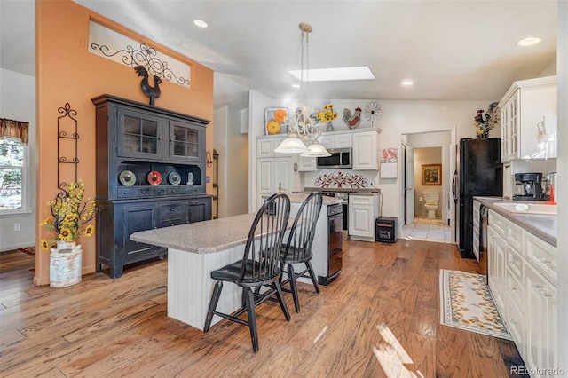 kitchen featuring white cabinetry, vaulted ceiling with skylight, pendant lighting, a kitchen bar, and light tile patterned floors