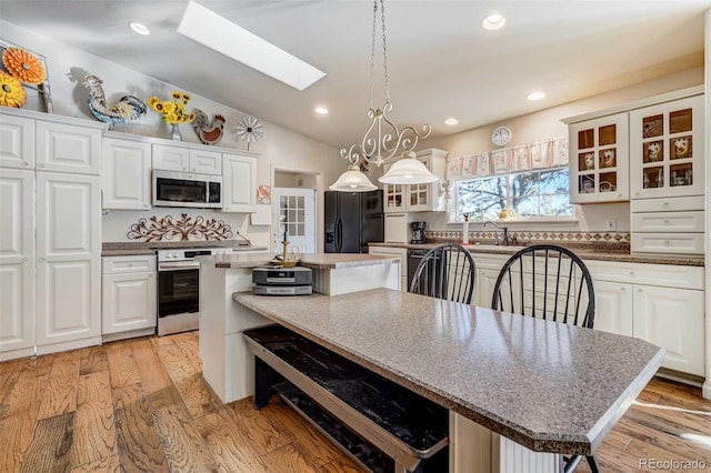 kitchen featuring black refrigerator with ice dispenser, light wood-type flooring, vaulted ceiling with skylight, and a kitchen island