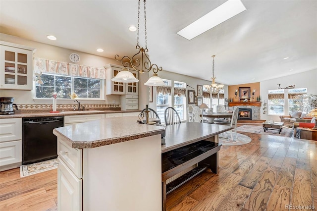 kitchen with hanging light fixtures, a skylight, sink, black dishwasher, and light hardwood / wood-style floors