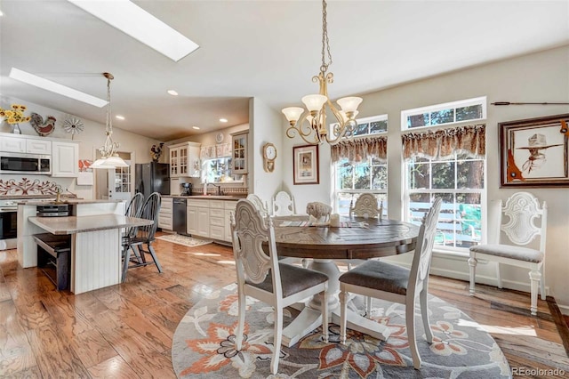 dining area featuring lofted ceiling with skylight, light hardwood / wood-style floors, sink, and an inviting chandelier