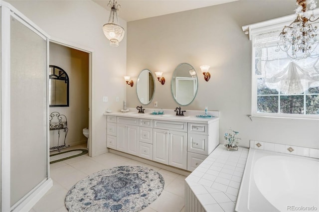 bathroom featuring tiled tub, tile patterned floors, dual vanity, and toilet