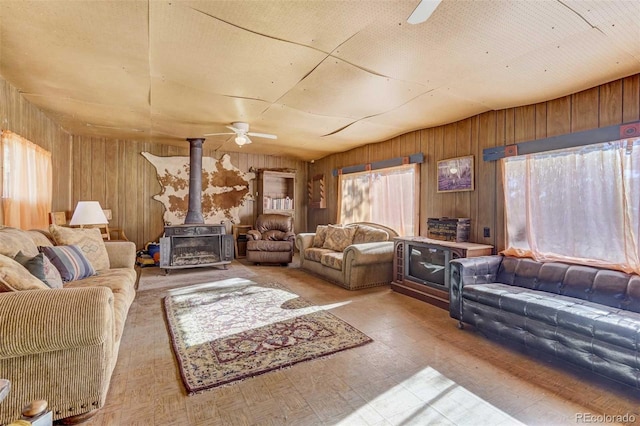 living room with a wood stove, wooden walls, a wealth of natural light, and ceiling fan