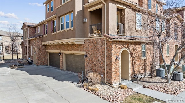 exterior space with central AC unit, stucco siding, a balcony, a garage, and driveway