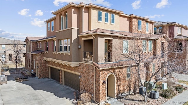 view of front of house featuring central AC unit, stucco siding, a garage, stone siding, and a tile roof