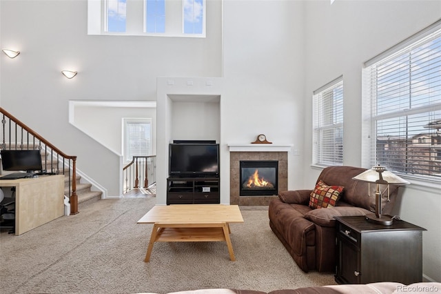 carpeted living room featuring stairway, plenty of natural light, a towering ceiling, and a tiled fireplace