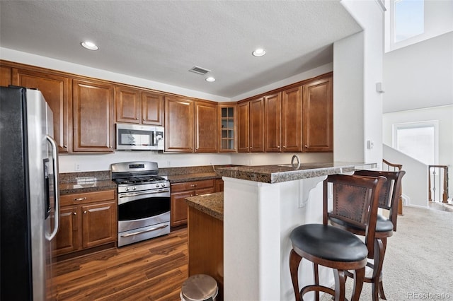 kitchen with visible vents, glass insert cabinets, a breakfast bar area, a peninsula, and stainless steel appliances