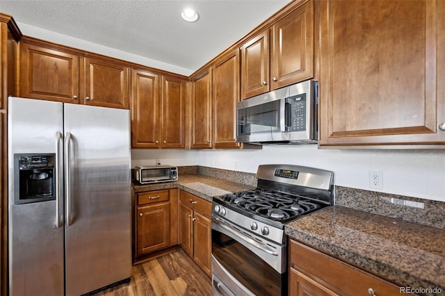 kitchen featuring brown cabinets, a textured ceiling, dark wood finished floors, stainless steel appliances, and a toaster