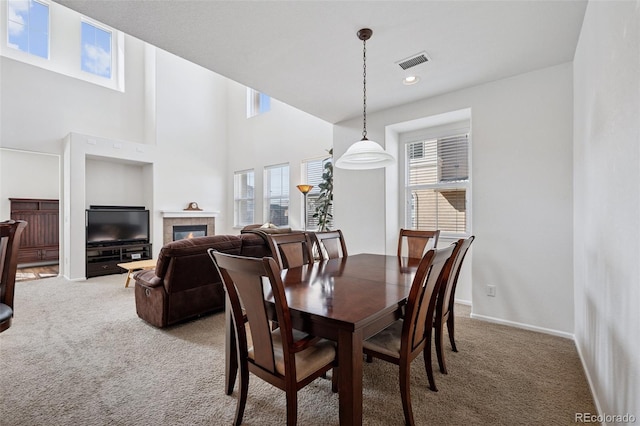 carpeted dining area with visible vents, recessed lighting, a high ceiling, a fireplace, and baseboards