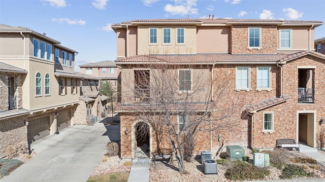 multi unit property with concrete driveway, a tile roof, stucco siding, stone siding, and an attached garage