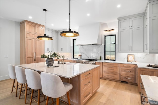 kitchen featuring backsplash, custom exhaust hood, a large island with sink, light hardwood / wood-style flooring, and hanging light fixtures