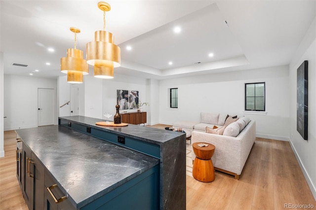 kitchen featuring a raised ceiling, light hardwood / wood-style flooring, a center island, and hanging light fixtures