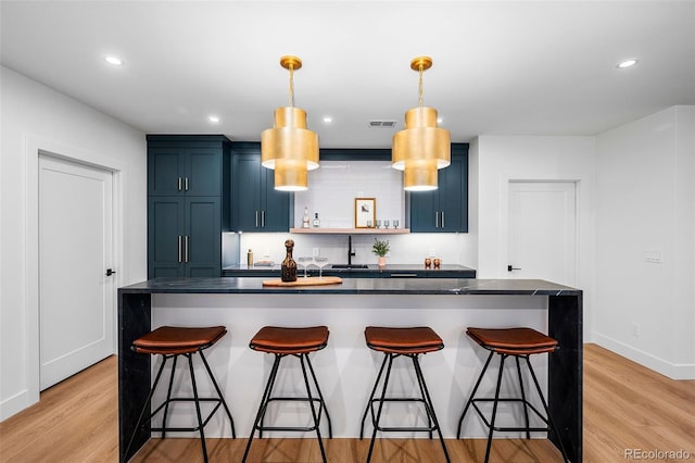 kitchen featuring a kitchen bar, light wood-type flooring, decorative light fixtures, and blue cabinets