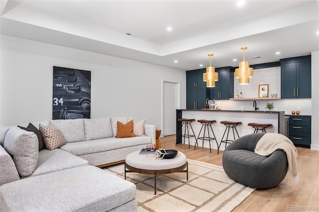 living room with a tray ceiling, light hardwood / wood-style flooring, and sink