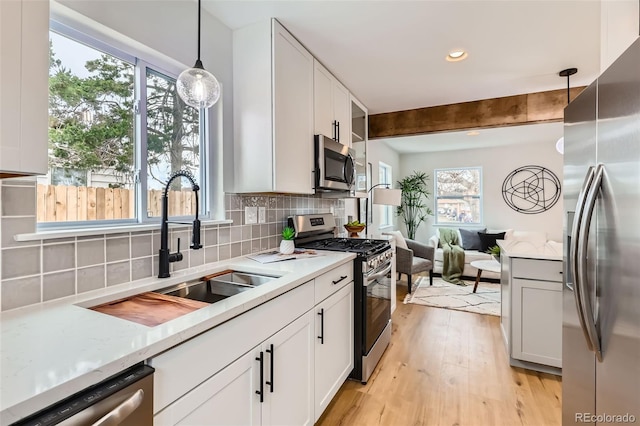 1120 Xenia St, Denver, CO 80220 - kitchen with backsplash, beam ceiling, light wood-style flooring, appliances with stainless steel finishes, and a sink