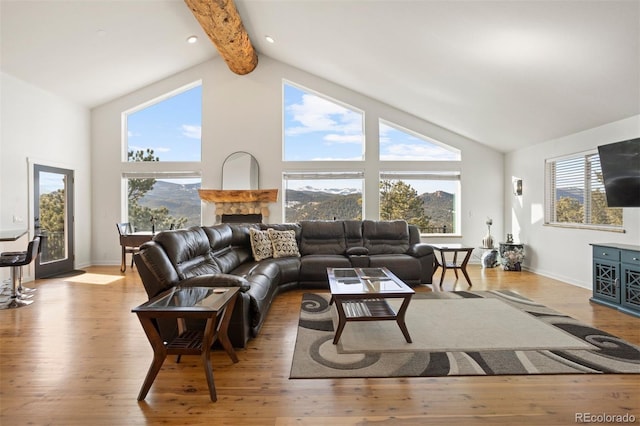 living room featuring beam ceiling, light wood-type flooring, high vaulted ceiling, and a stone fireplace