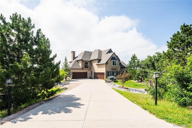 view of front of property featuring concrete driveway, stone siding, a chimney, an attached garage, and stucco siding