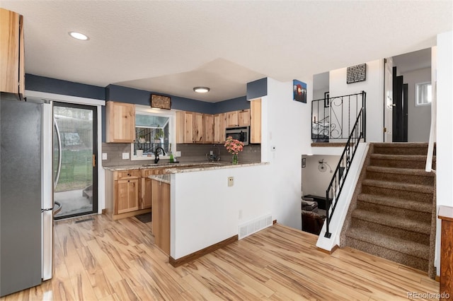 kitchen with appliances with stainless steel finishes, a sink, light wood finished floors, light brown cabinets, and visible vents