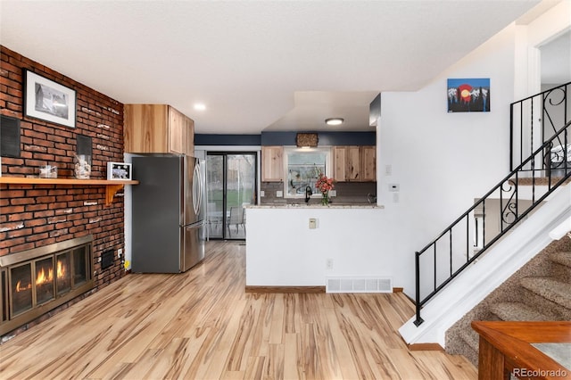 kitchen featuring a sink, light countertops, light wood-style flooring, freestanding refrigerator, and visible vents
