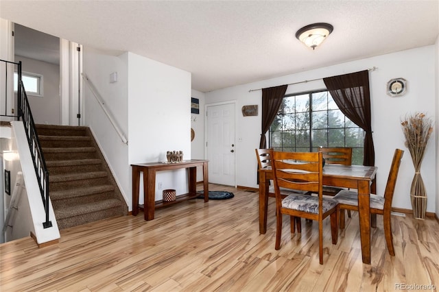 dining area with stairs, a textured ceiling, baseboards, and light wood finished floors