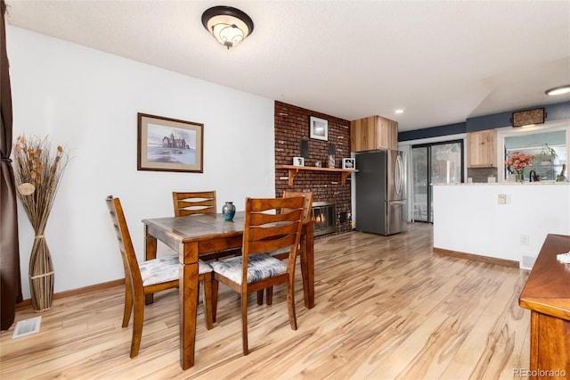 dining space featuring baseboards, a brick fireplace, light wood-style flooring, and visible vents
