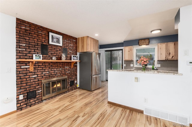 kitchen with light brown cabinetry, a brick fireplace, light wood-style flooring, freestanding refrigerator, and visible vents