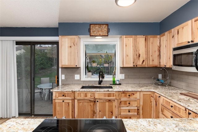 kitchen featuring a sink, stainless steel microwave, light brown cabinetry, and tasteful backsplash