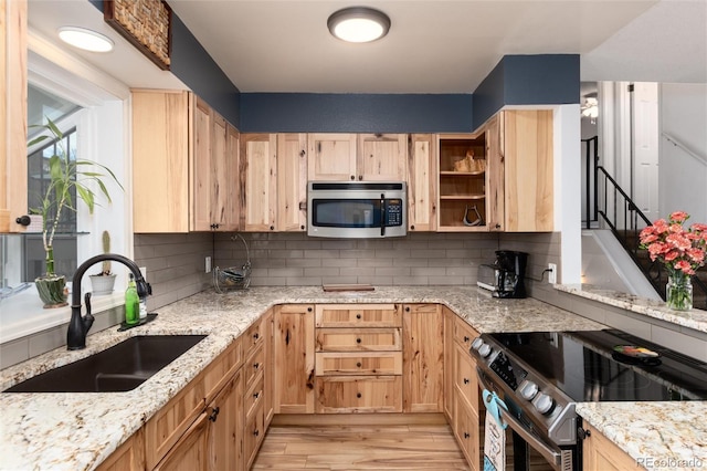 kitchen with light brown cabinetry, light stone countertops, appliances with stainless steel finishes, a sink, and light wood-style flooring