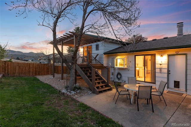 back of house at dusk with a patio area, stairway, fence, a yard, and a shingled roof