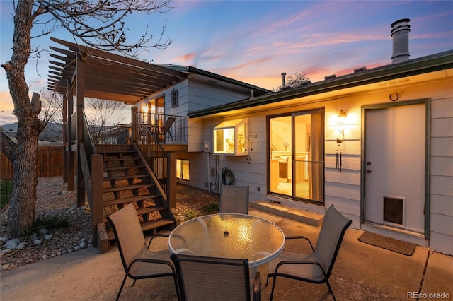 patio terrace at dusk with fence, outdoor dining space, stairway, and a wooden deck