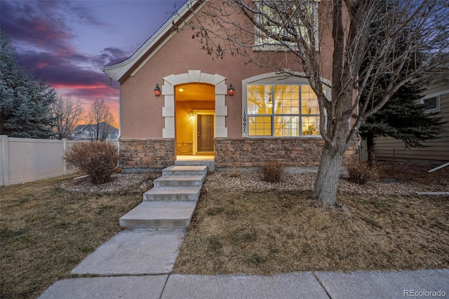 view of front of home with a front yard, stone siding, fence, and stucco siding